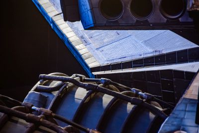 From a vantage point beneath the trailing edge of the orbiter's right wing, you are looking up and across at the rear end of the Space Shuttle Atlantis. Along the top right of the image, you can see three of the Reaction Control System motors, and along the lower left of the image, two of the Space Shuttle Main Engines can be seen. In the background between them, the speed brakes along the trailing edge of the vertical stabilizer can be seen in their retracted position, folded together, side by side, in near contact with one another.